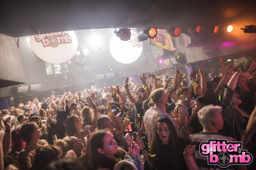 A packed crowd with hands in the air under coloured lights